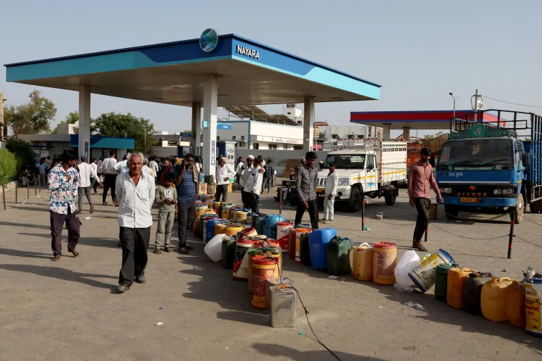 Villagers stand near plastic containers at a fuel station to fill their water pumps, as India faces rising oil prices, in Halvad, Gujarat, India