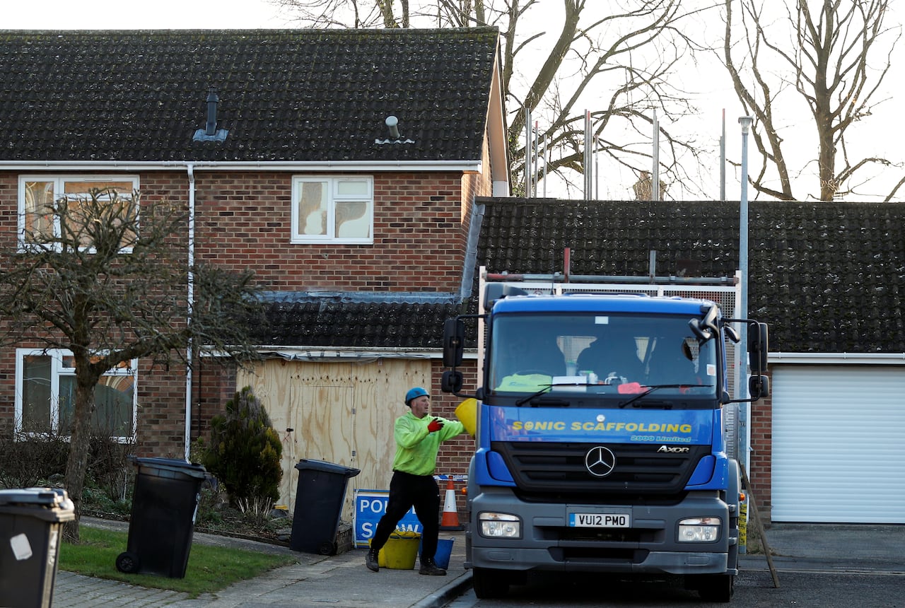 A man loads material into a truck in front of a two-storey brick house.