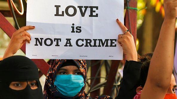 A woman with her face and head covered holds up a poster that says "Love is not a crime"