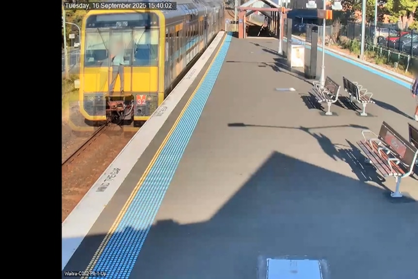 A boy stands up on the buffer of a train that is passing through a station.
