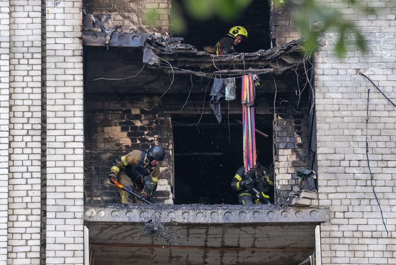 Firefighters shovel away debris from an apartment where the exterior wall has collapsed.