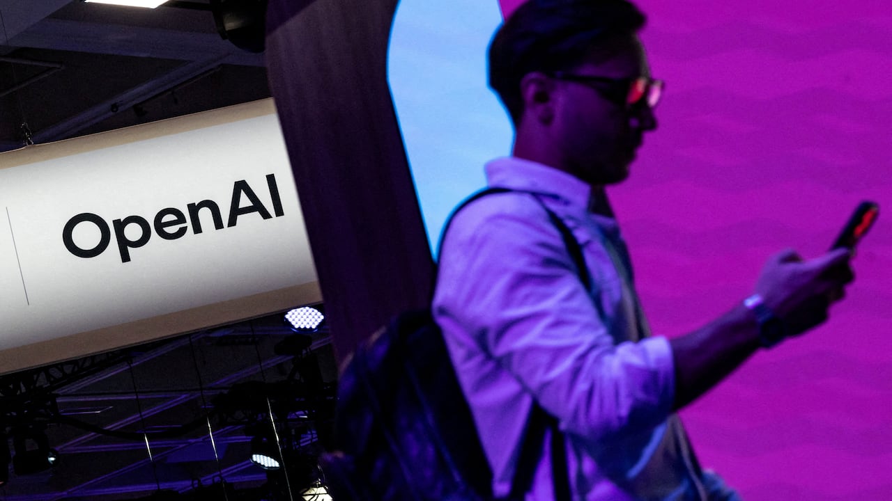 Man holding phone walks by logo for OpenAI on poster