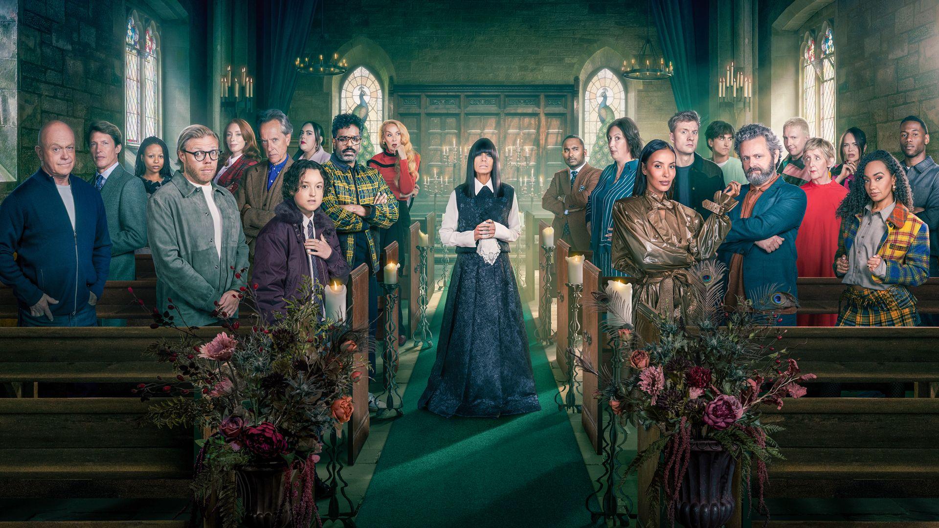 The Celebrity Traitors 2 constestants all lined up inside the castle, either side of host Claudia Winkleman. They are standing in wooden pews, while Claudia stands in the aisle running down the middle, wearing a black dress with white sleeves and collar. 