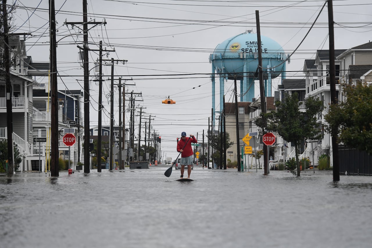 A person on a paddleboard navigates a flooded street.
