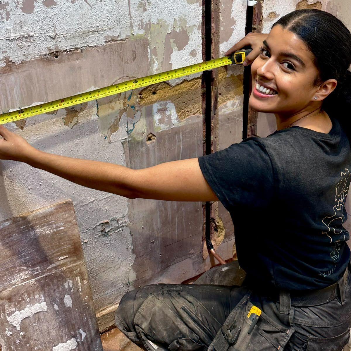 Bliss Cunneen holds a tape measure up to a wall and smiles at the camera. 