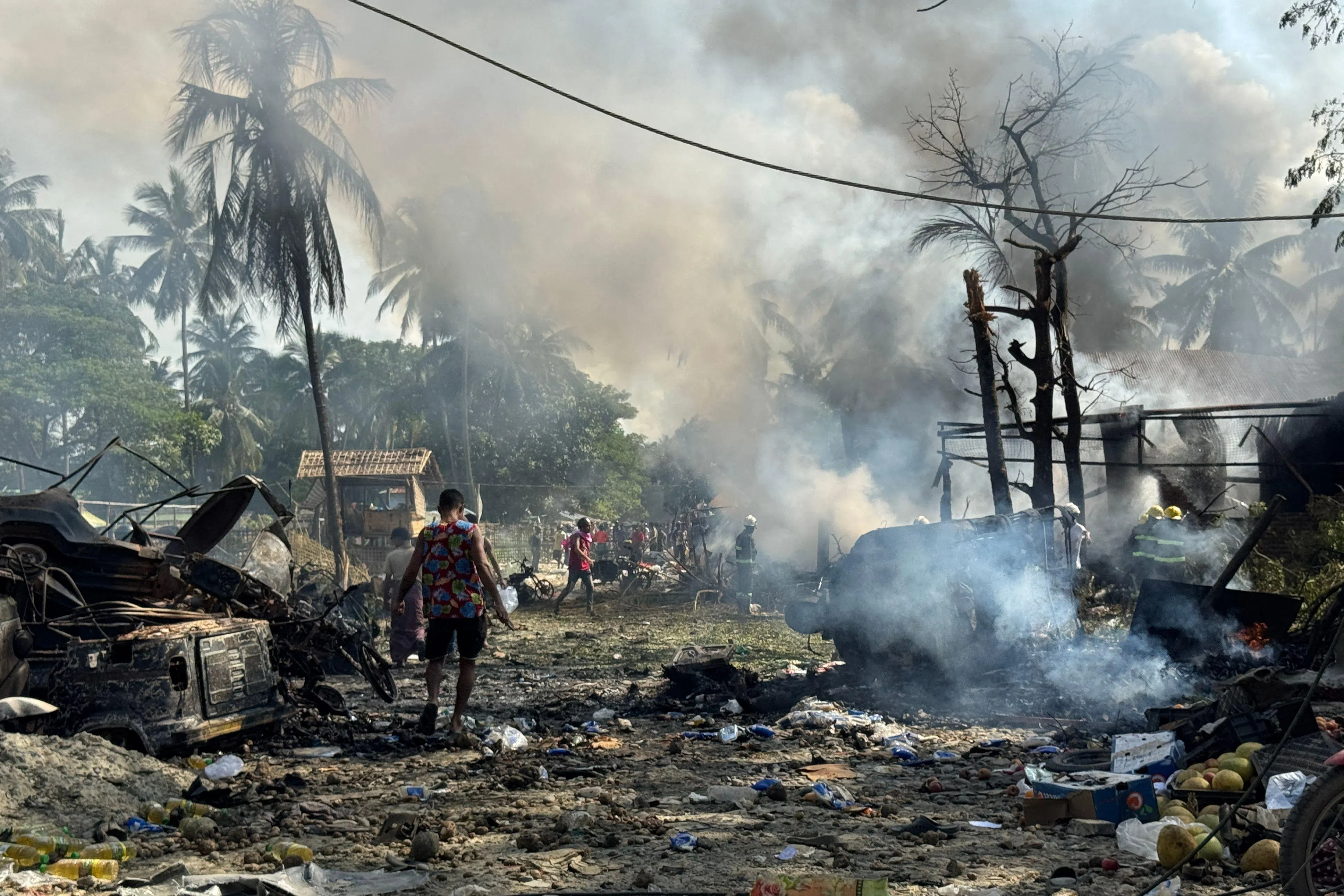 People walk through smoke and smouldering debris following a military airstrike on a market and adjacent bridge in Kyauktaw, Western Rakhine state on September 28, 2026. A military airstrike on a market in western Myanmar killed 33 people on September 28 and wounded 36 more, a rebel faction which controls the area said in a statement. (Photo by AFP)