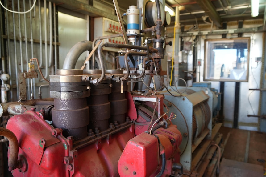 A red steam engine, connected to an alternator and DC generator in an equipment room. 