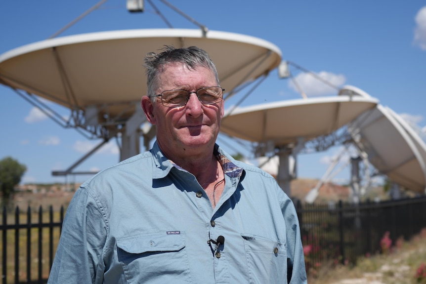 Rob Dyson standing in the sun with the parabolic dishes of the solar station pointing at the sky in the background