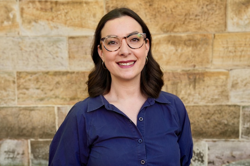 Alexandra Boukouvalas standing in front of a sandstone wall and smiling directly at the camera