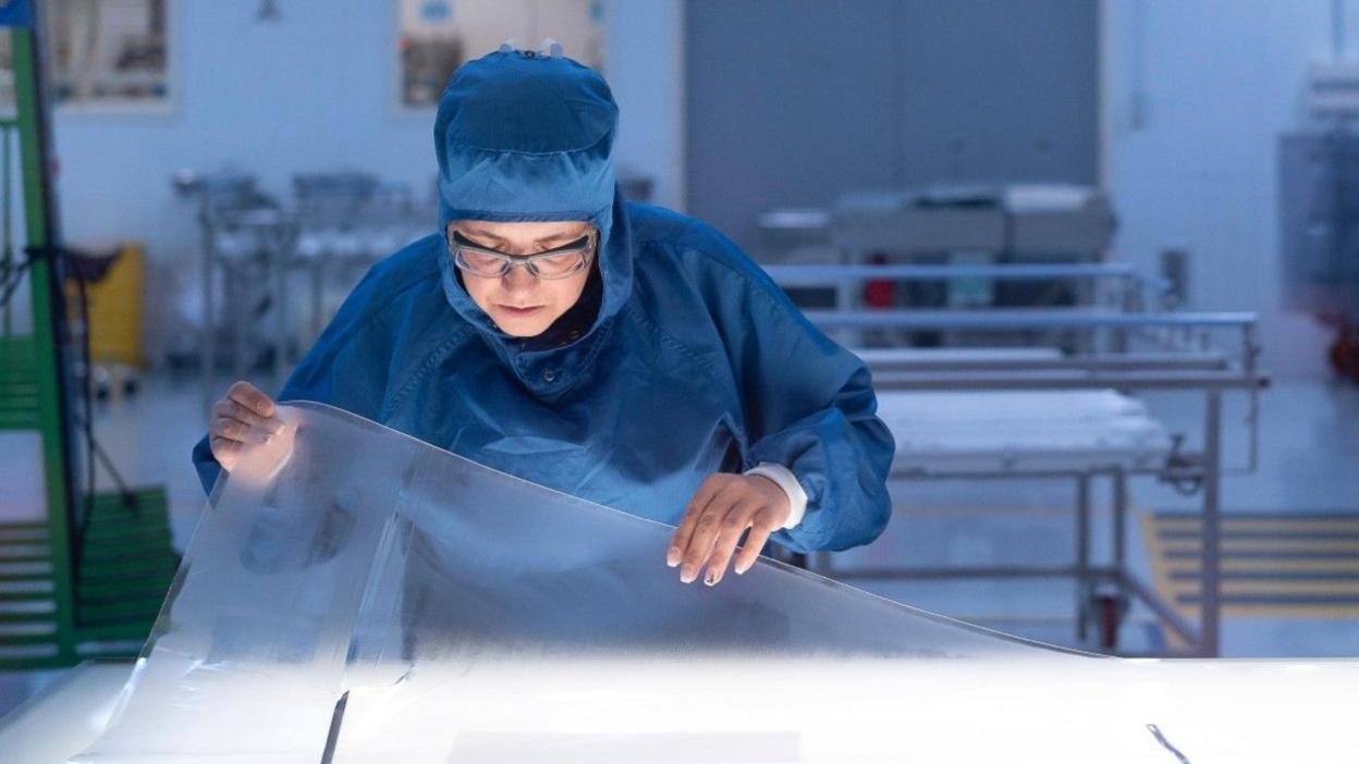 A Saint-Gobain worker in a darkened room works on a clear sheet of acrylic.