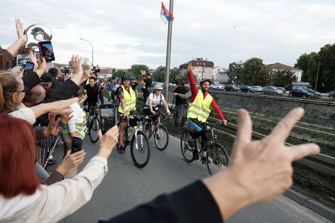 Cyclists gesture as they are meet by spectators.