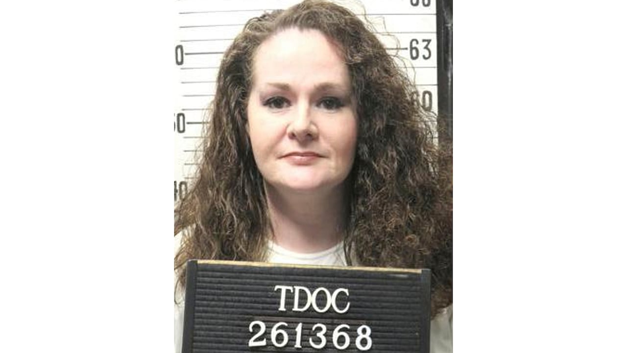 A woman holds a black Tennessee Department of Correction board with a number on it, in a mug shot.