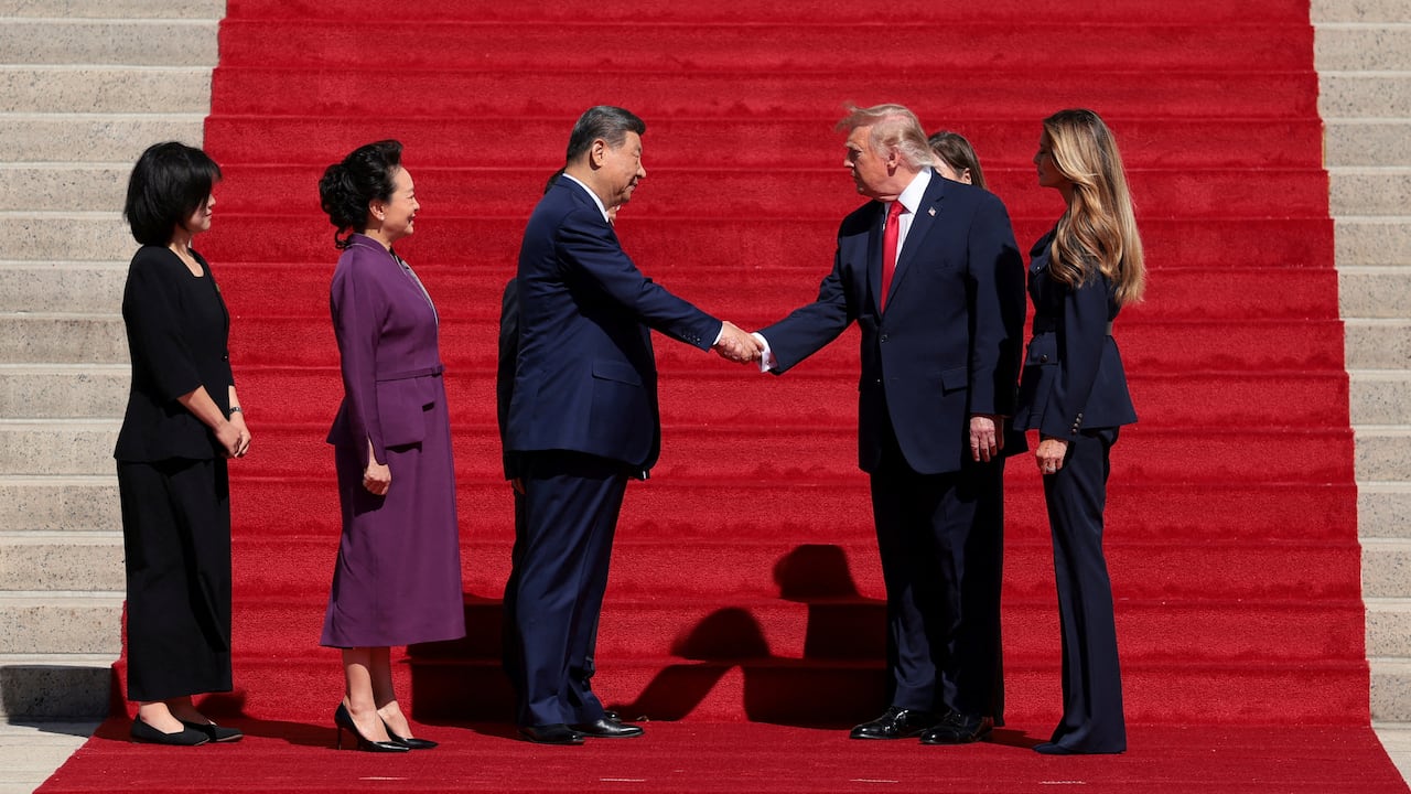Two men in suits shake hands on a red carpet.