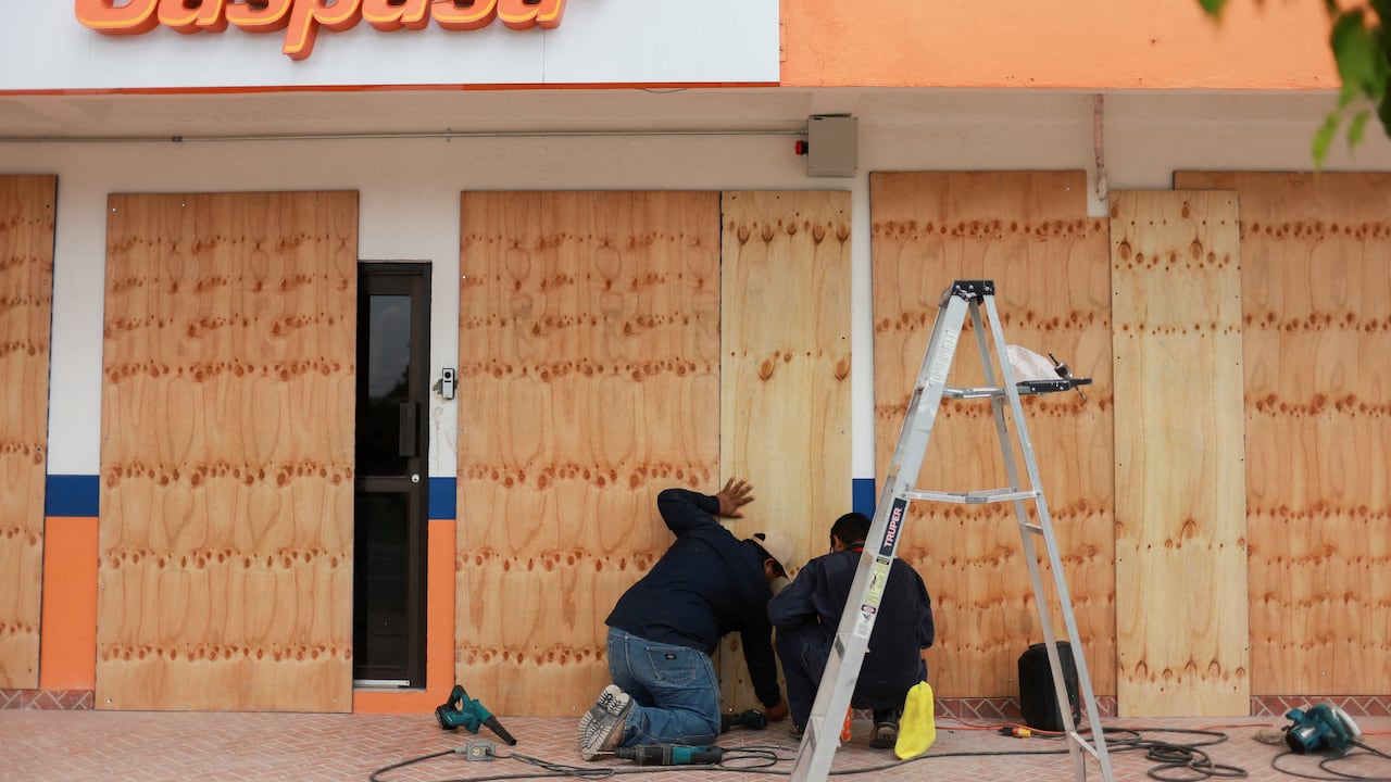 People board up glass windows at a gas station in anticipation of a hurricane.