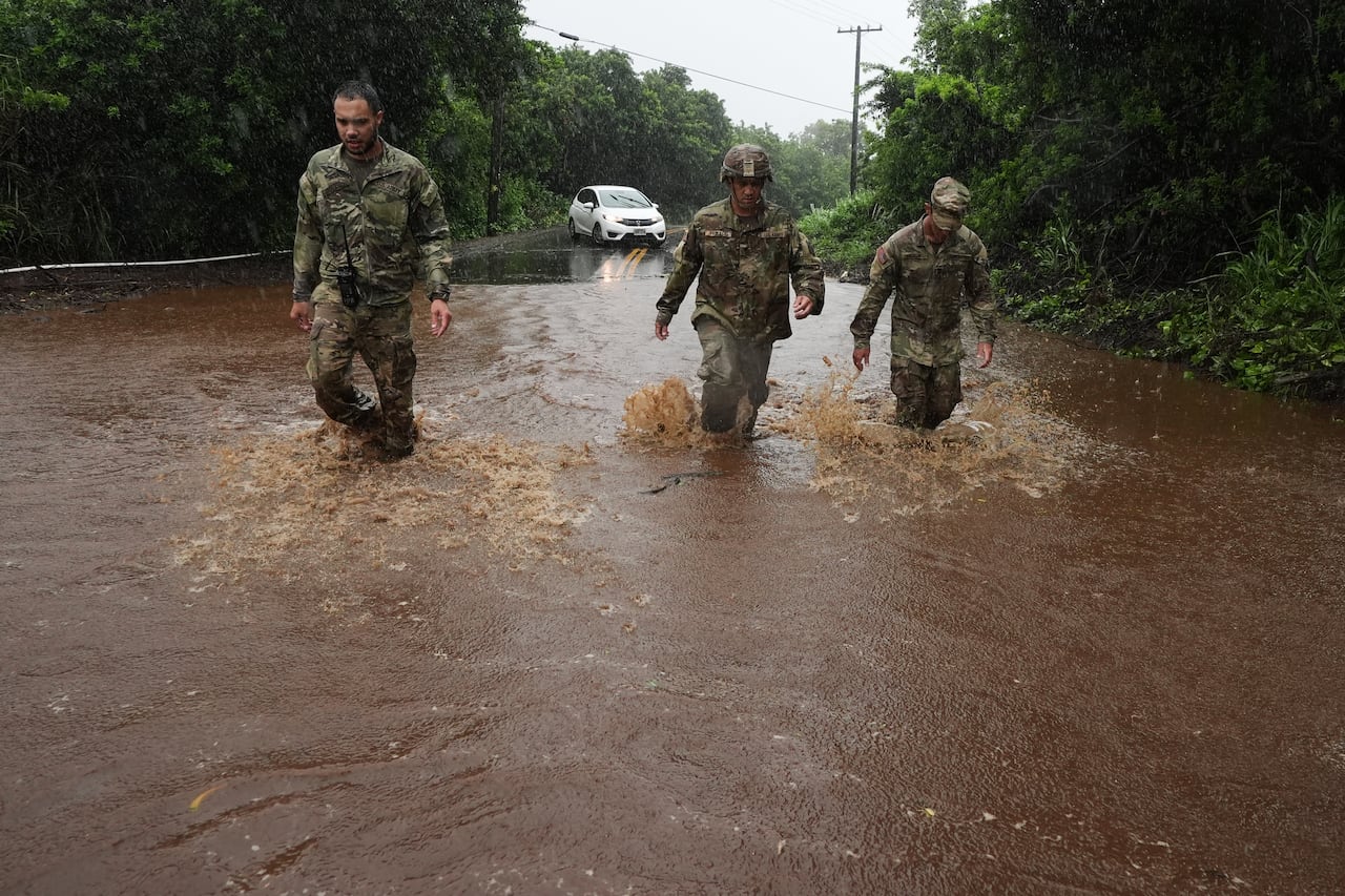 Soldierse walk though heavy rainwater on a paved road.