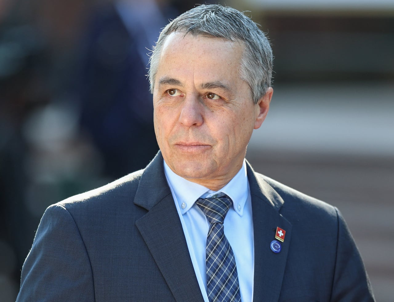A man in a suit and salt and pepper hair stares on.