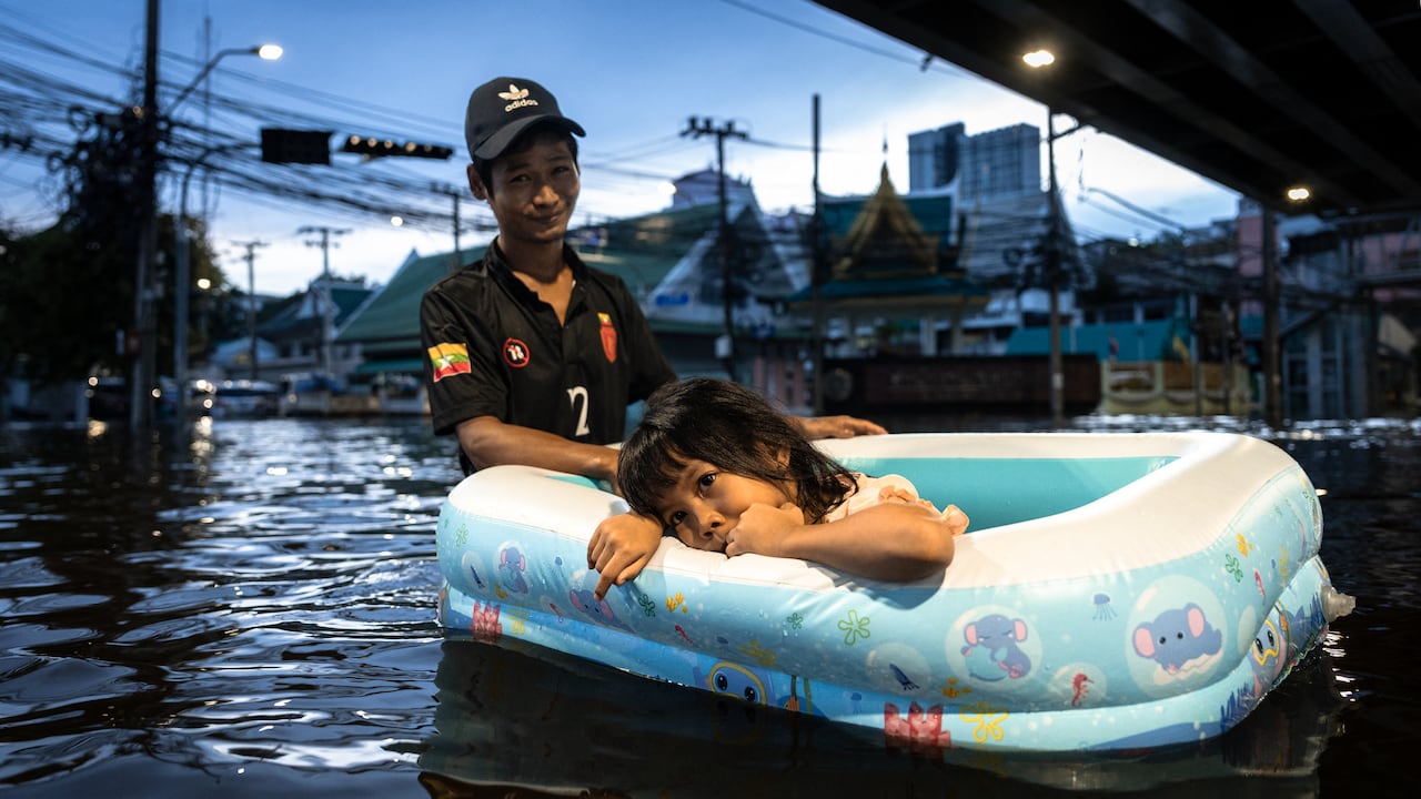A man in hip-deep water, with a small girl resting her head on the side of what it appears to be a small inflatable pool, at twilight.