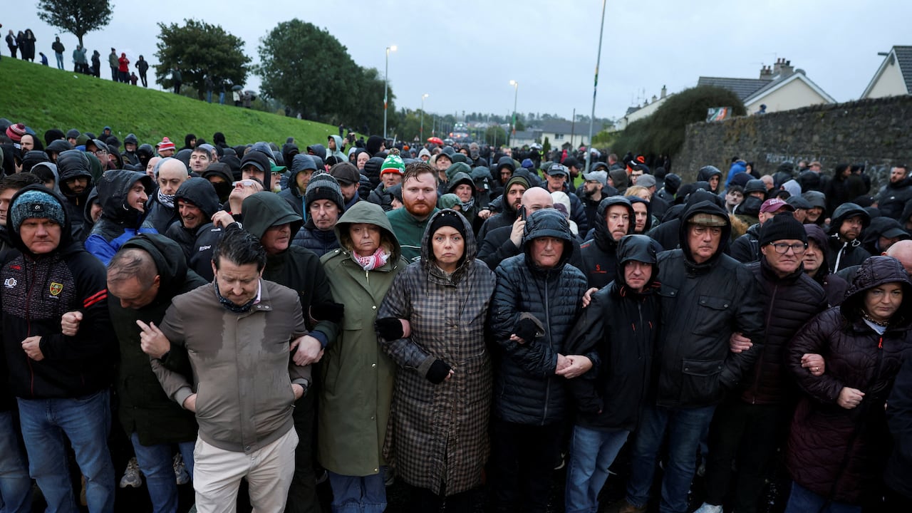 A large crowd lock arms on a road on a rainy day.