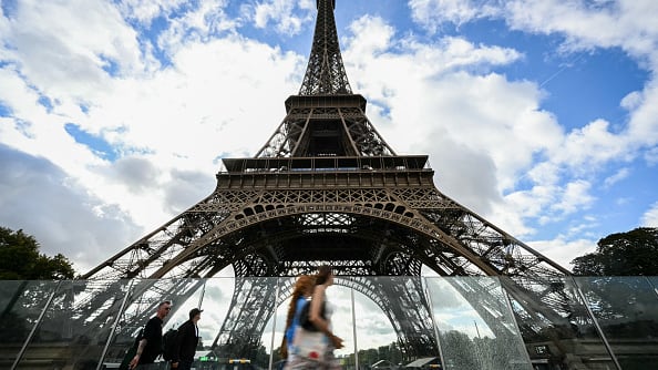 Pedestrians walk near the Eiffel Tower in Paris on a sunny day.