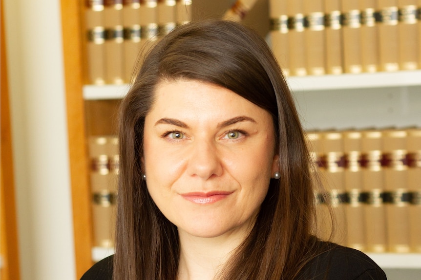 A woman with brown hair wearing black standing in front of shelves of books.