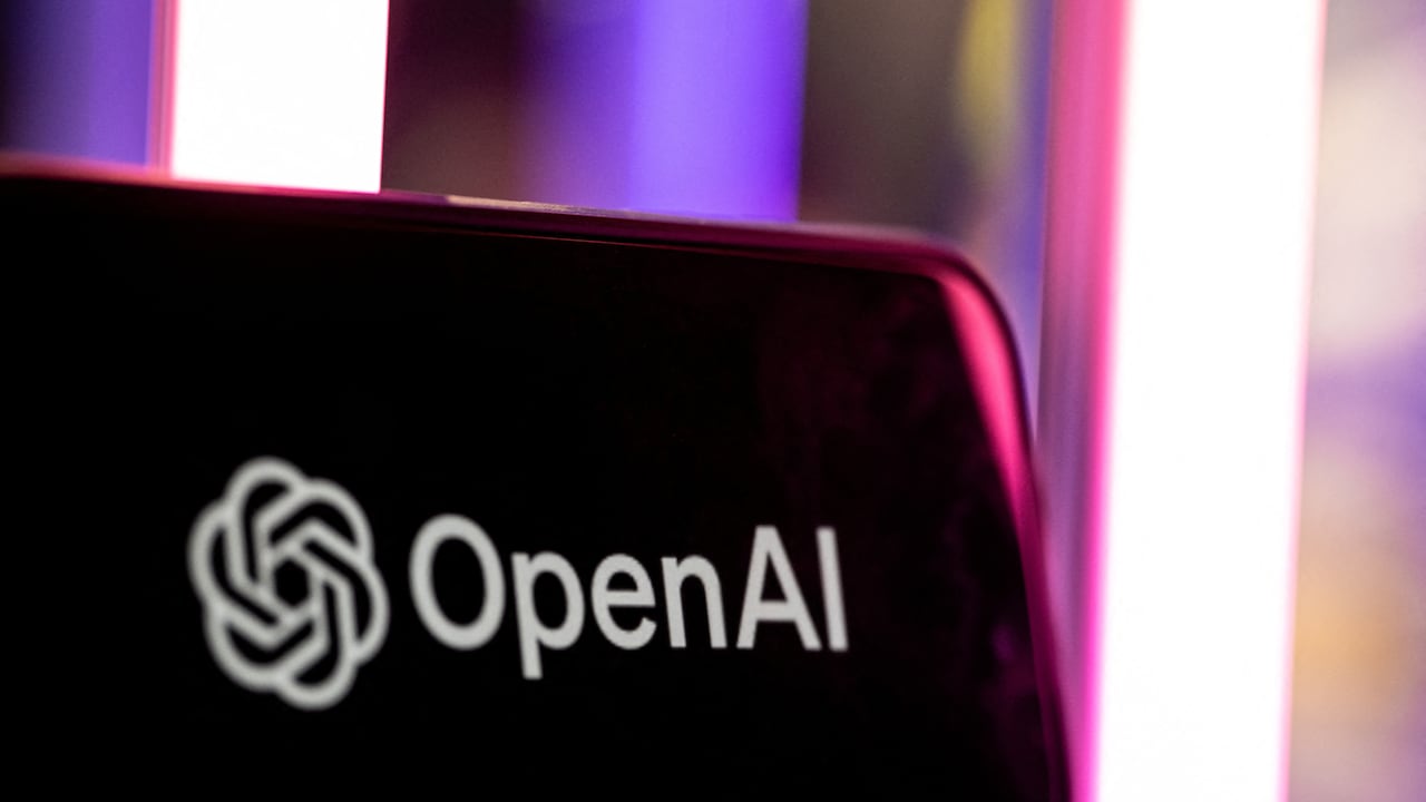 A smartphone with the OpenAI logo is seen against a backdrop of purple to yellow-tinged lights.