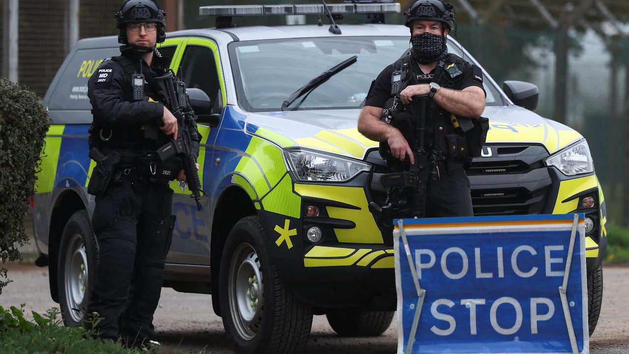 Two police officers in tactical gear stand beside a police car and sign that says Police Stop