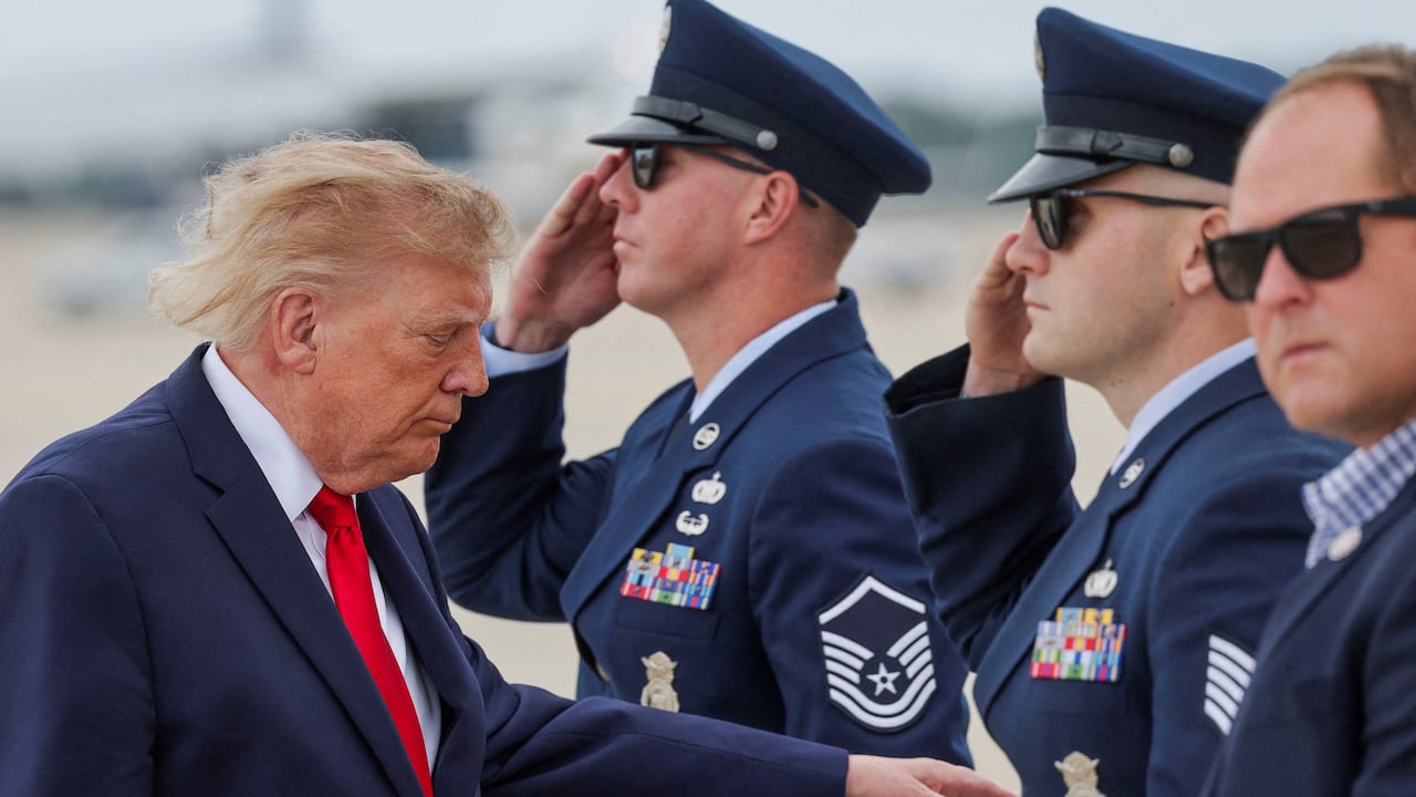 An old man with blond hair walks past soldiers on a tarmac.