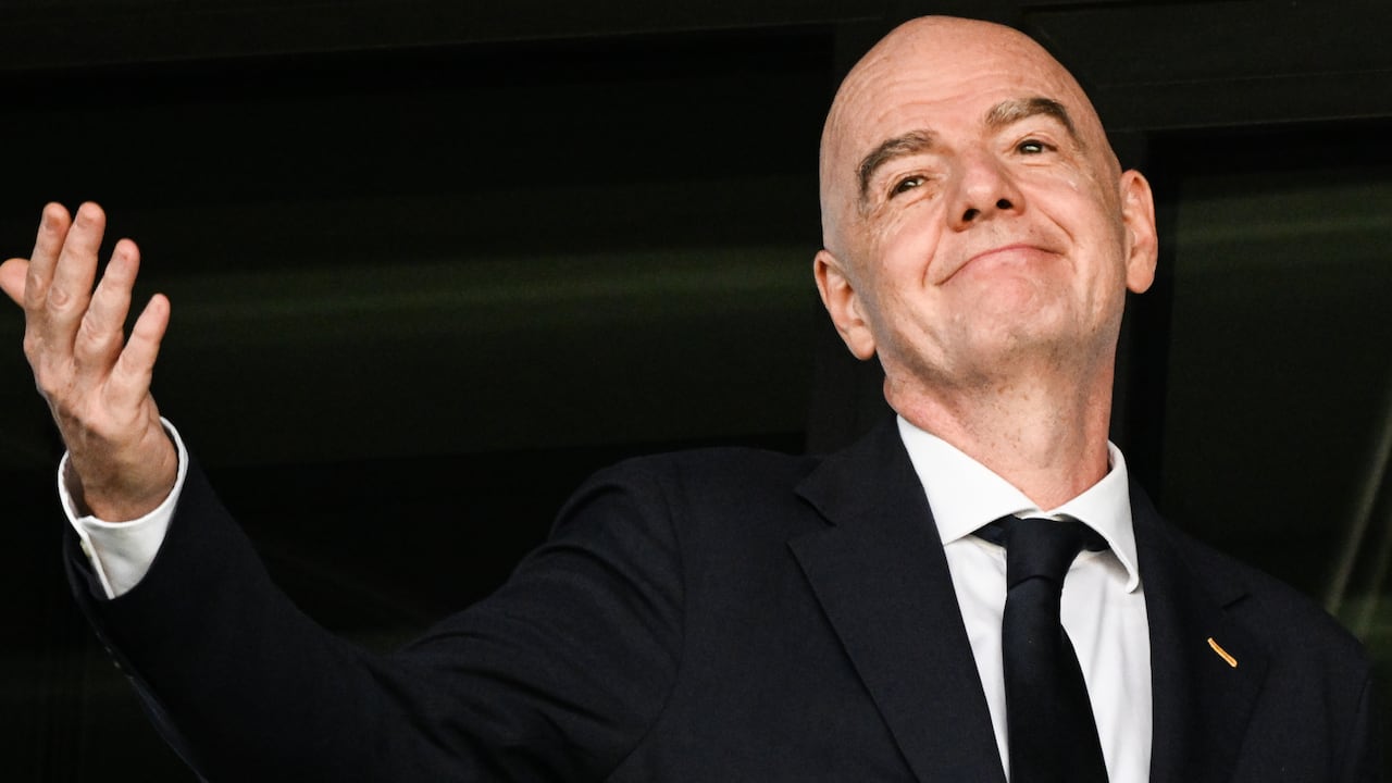 A man in a suit gestures with an upturned palm.