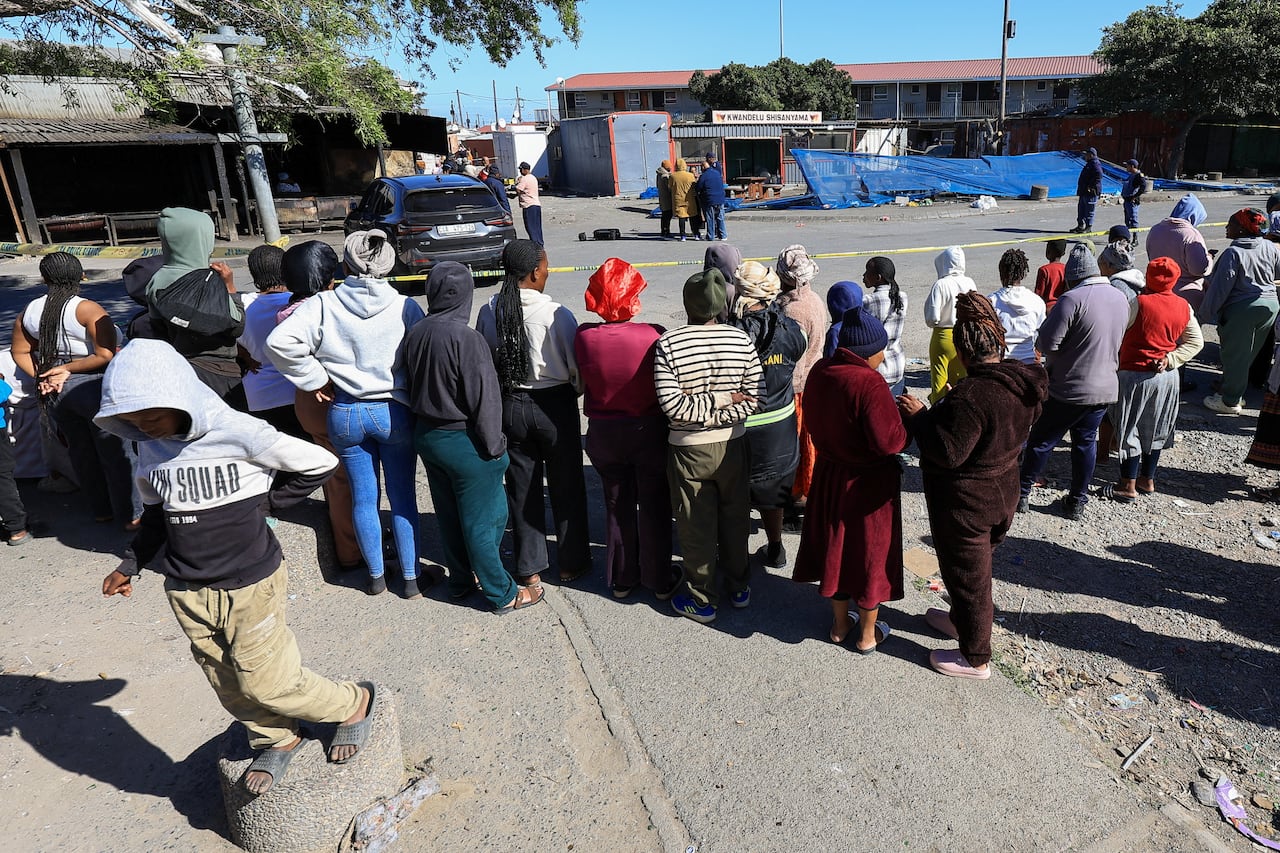 People stand outside a crime scene near houses.