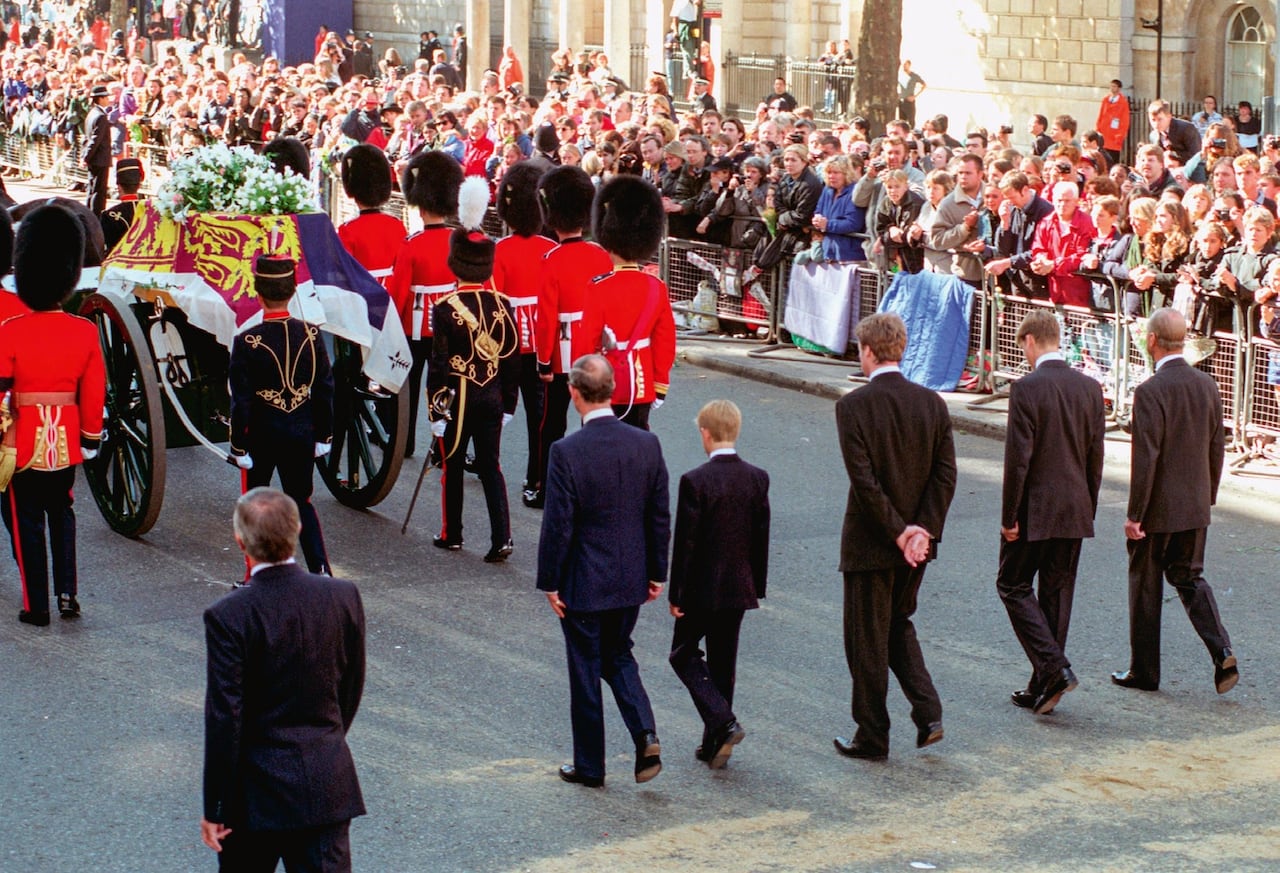 Men and children walk behind a coffin in a funeral procession, as crowds line the street