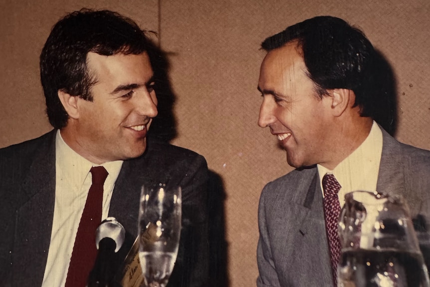 Two men sitting at a table share a laugh, with champagne