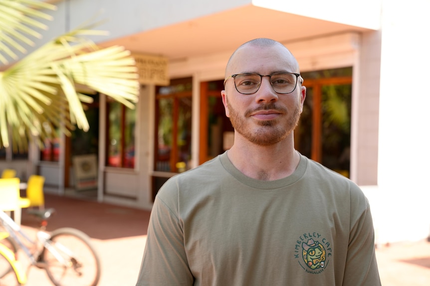 White bald man with glasses posing in front of a cafe