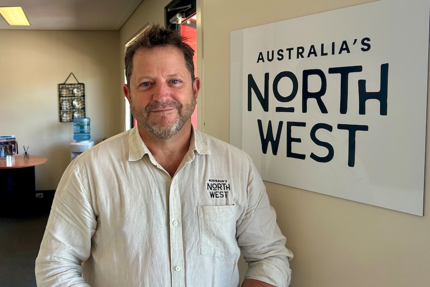 Man in white shirt smiles in front of sign reading Australia's North West.