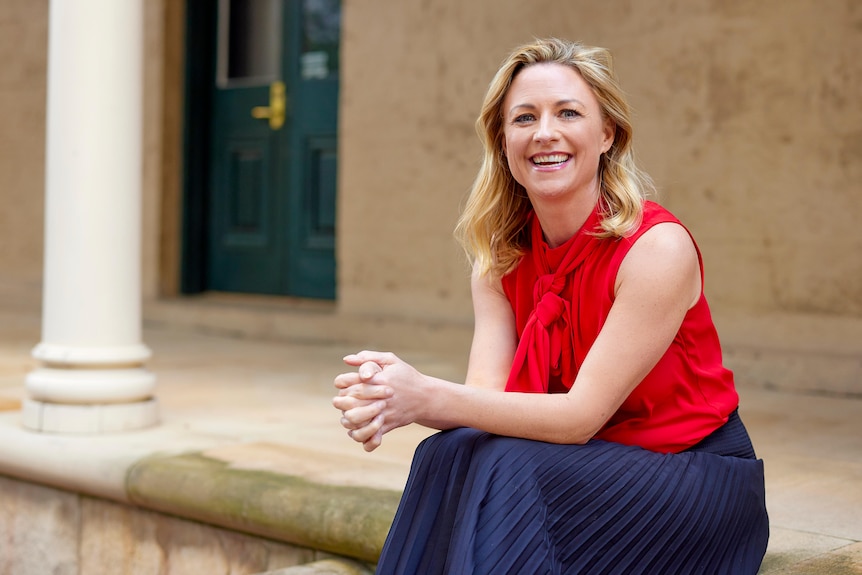 A woman sitting on a step, smiling at the camera with elbows resting on her knees and hands clasp together