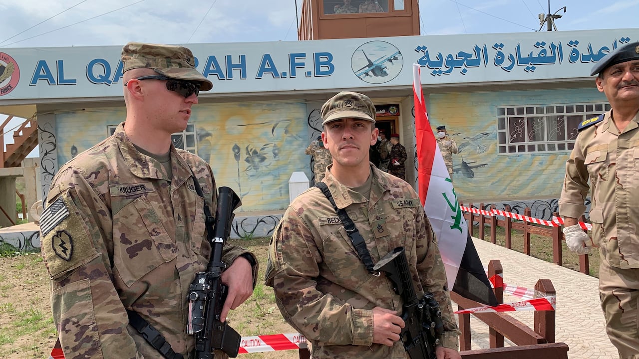 Apparent soldiers in caps and camouflage uniforms stand outdoors.