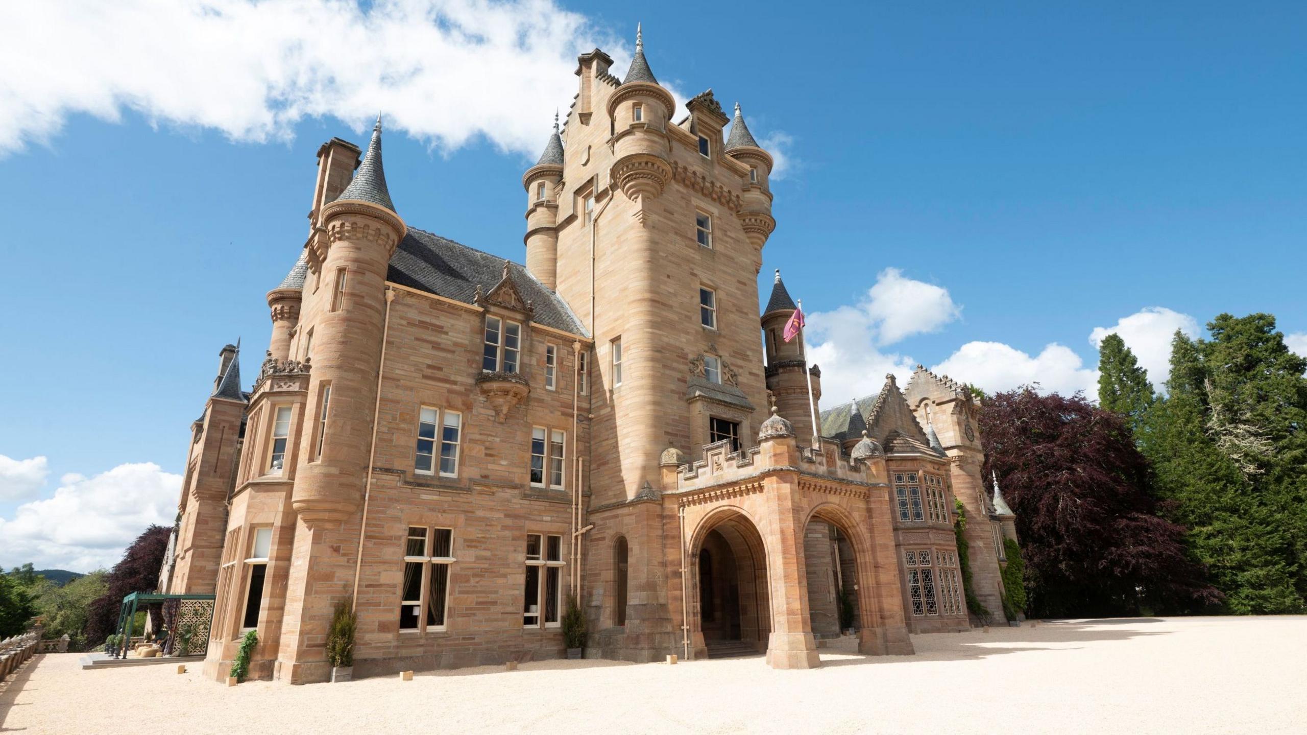 An exterior view of Ardross Castle, a sandstone-walled property in baronial style with turrets and faux battlements.