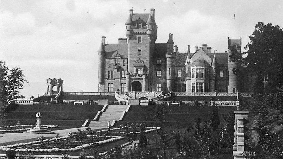 Ardross Castle in black and white photograph. It a large sandstone-walled property in baronial style with turrets and faux battlements.