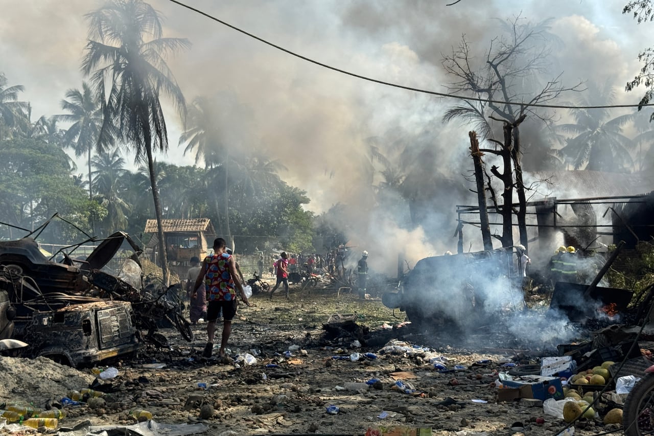 Smoke fills the air as charred vehicles and structures are shown in what appears to be a rural or jungle-like area.