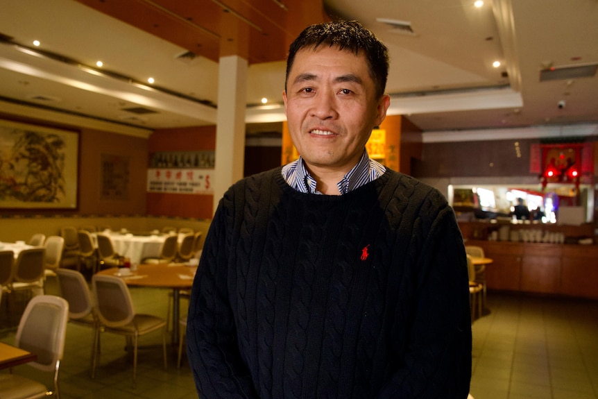 Valentine poses for a photo inside a restaurant, wearing a jumper.