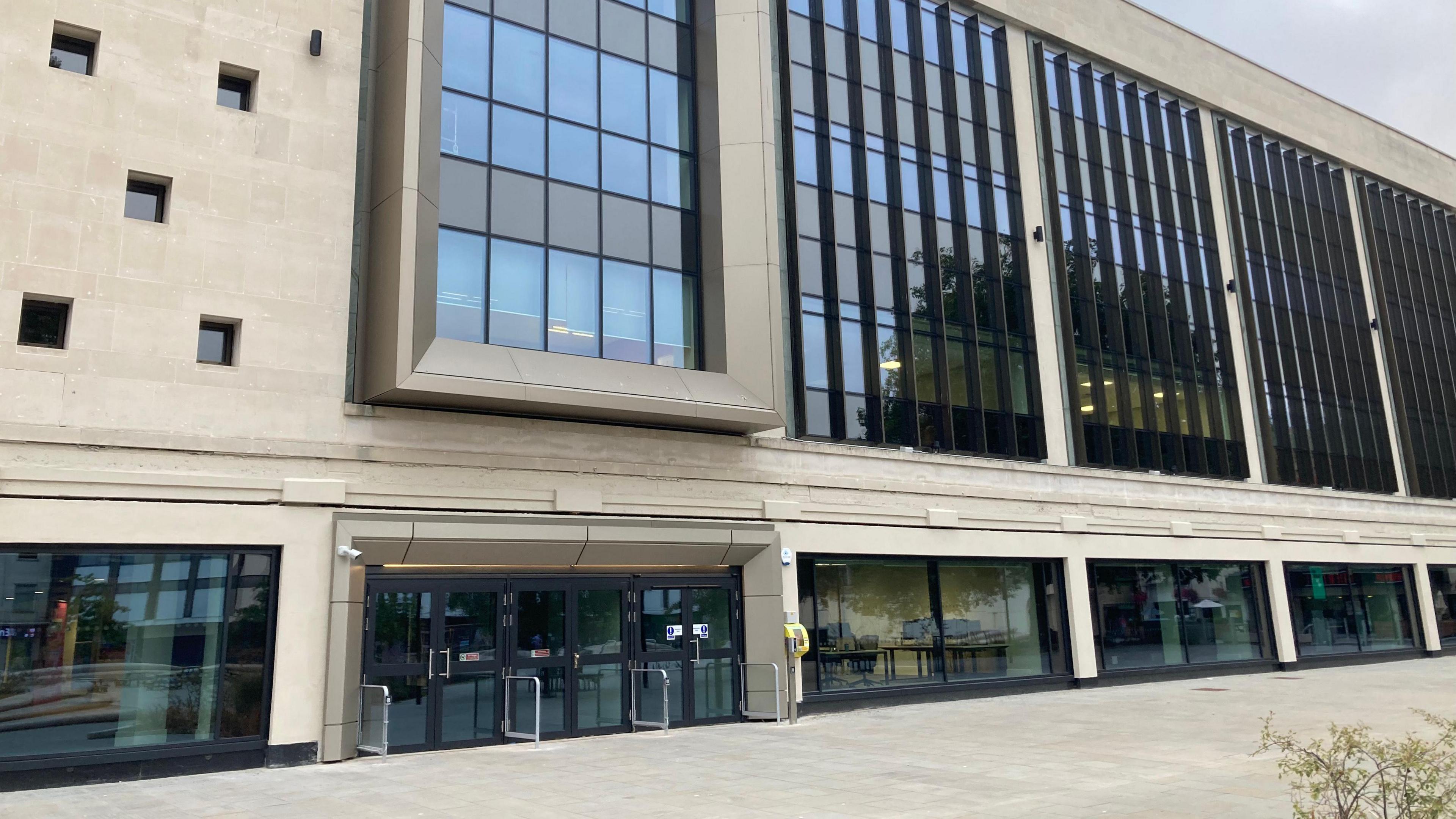 Exterior view of the newly redeveloped former Debenhams building in Gloucester, with a light modern façade, large windows and paved pedestrian area in front.

