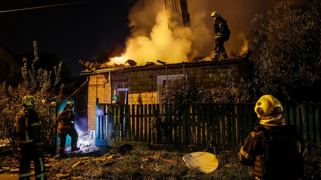 Firefighters work to extinguish a small house which is on fire at night.