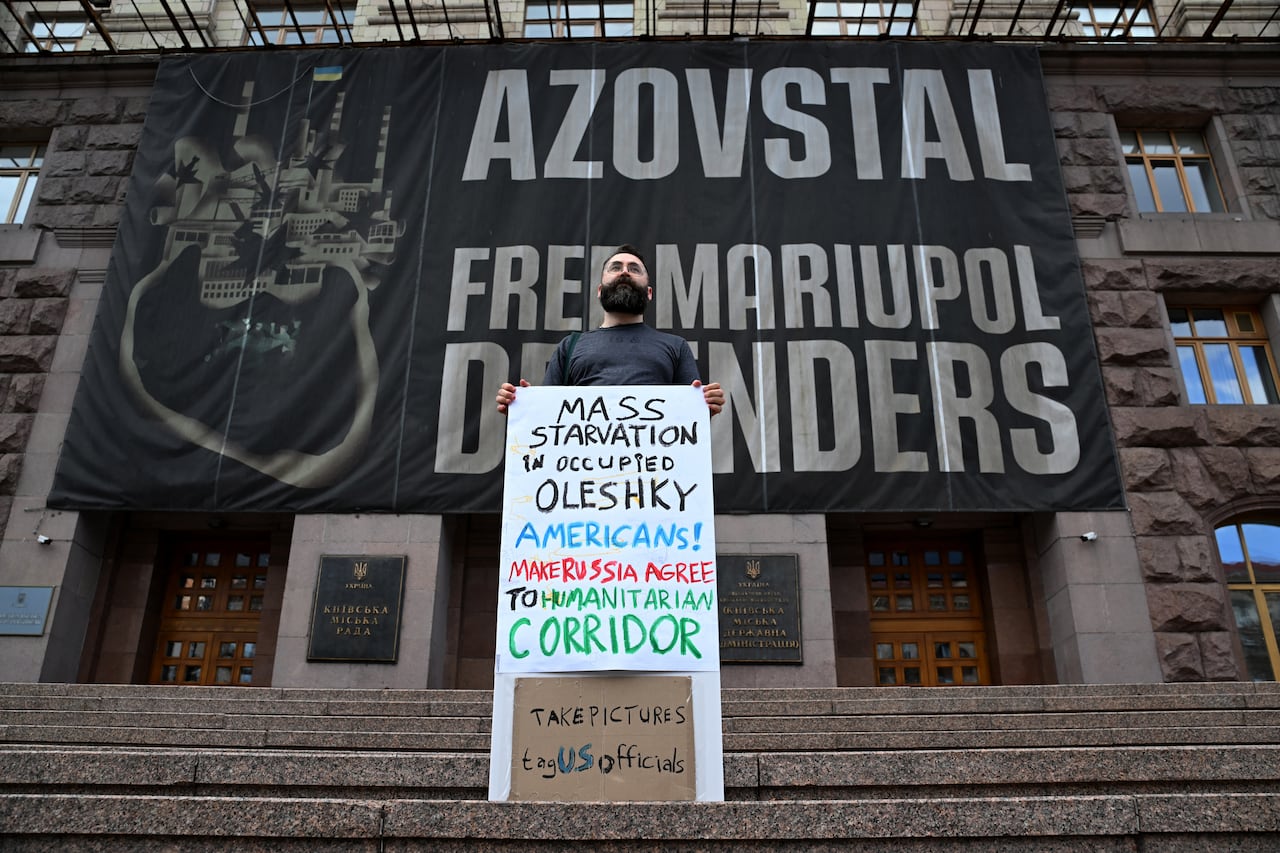 A man wearing a face mask holds up a placard reading "Mass starvation in occupied Oleshky. Americans! Make Russia agree to a humanitarian corridor".