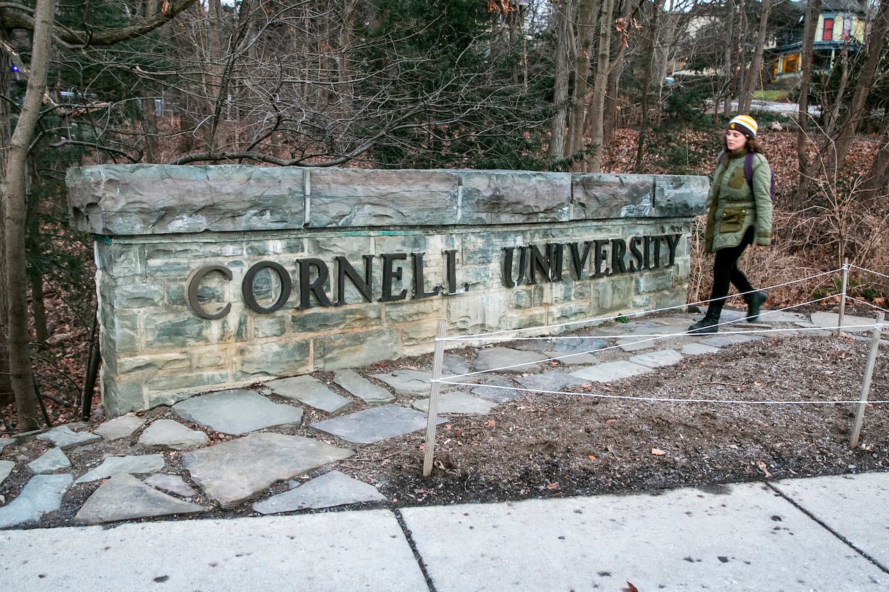 A woman walks past a sign that says Cornell University