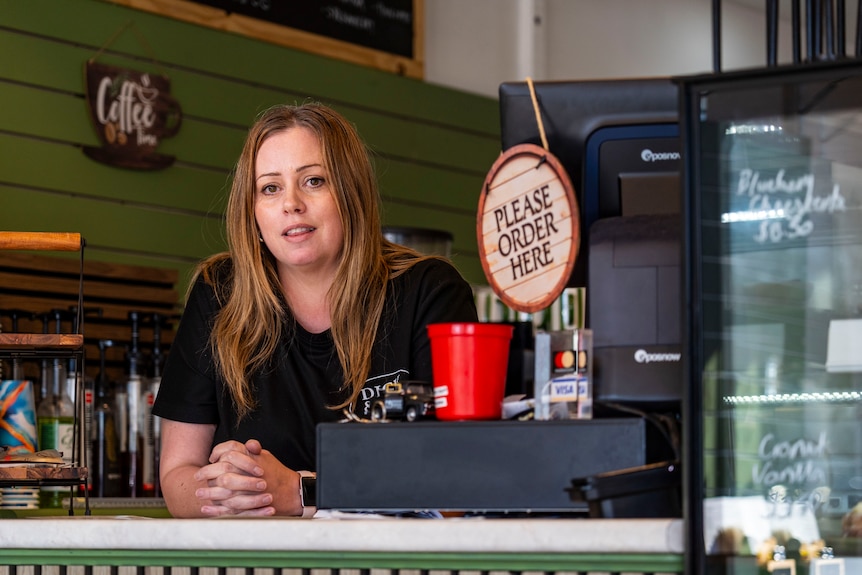 a woman with light brown hair and a dark shirt looks angry at the premises of a cafe