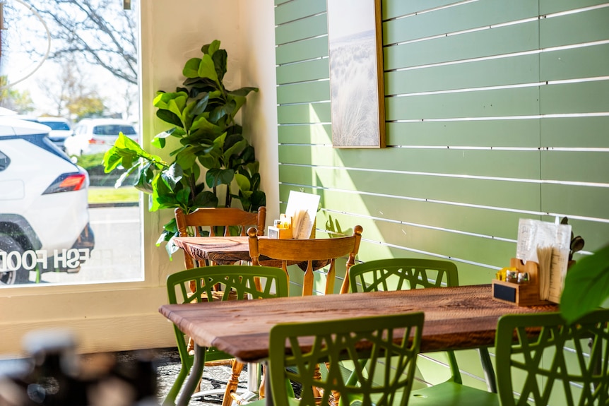 a green walled cafe filled with a coffee machine, equipment, dining chairs and food