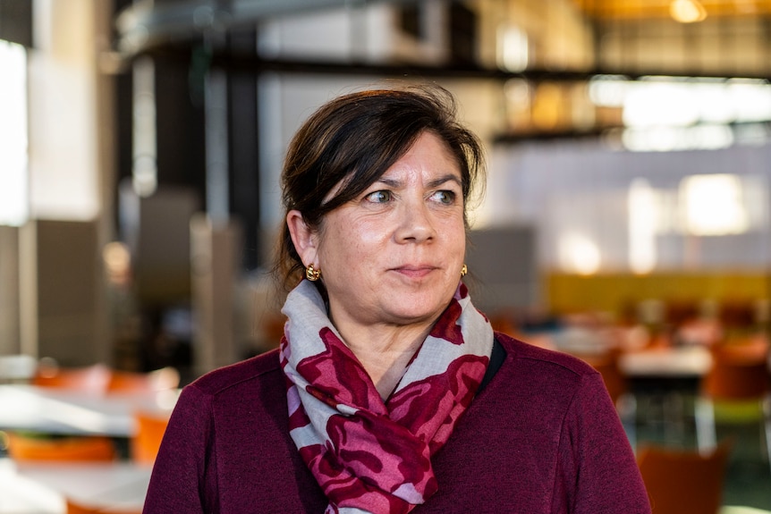 a brunette woman in a purple jumper with a scarf inside an event centre
