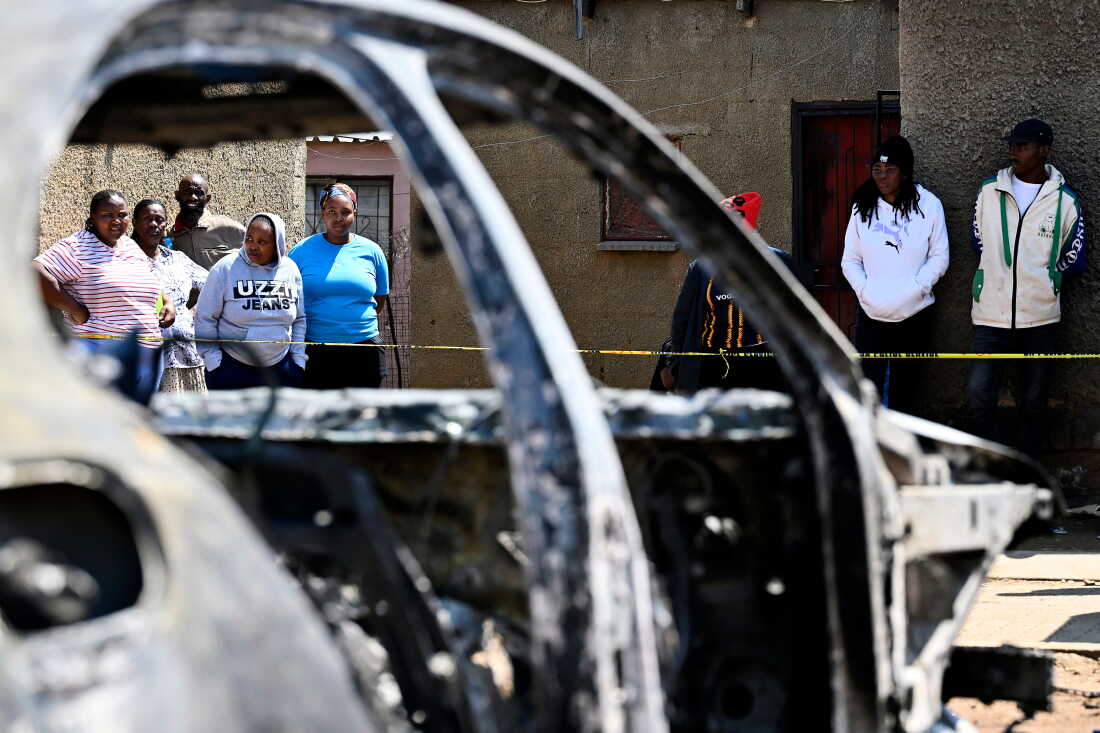 Community members stand at scene of a mass shooting on Saturday night when suspects opened fire at a bar in Wedela township, southwest of Johannesburg, South Africa, Sunday, Sept. 27, 2026.