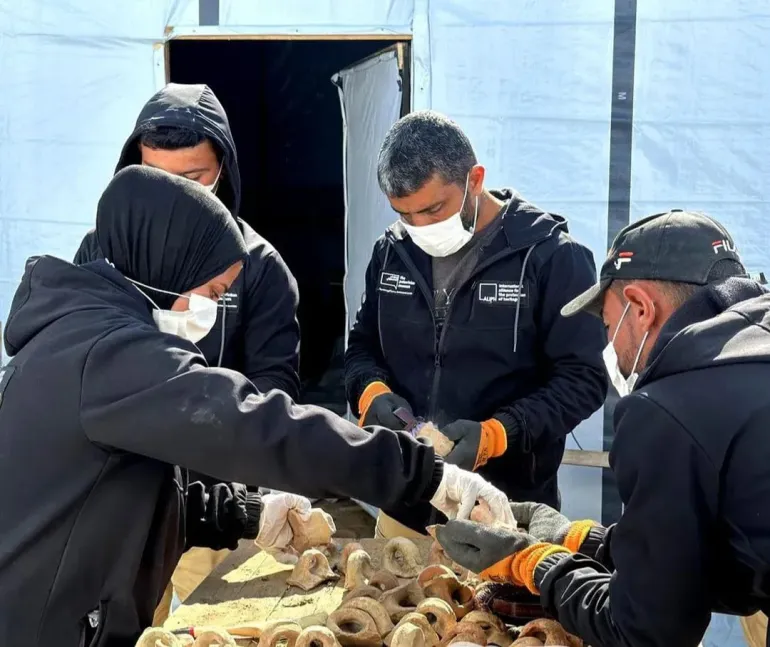 Members of the Guardians of Heritage team inspect and clean recovered archaeological pottery inside a temporary storage tent in al-Mawasi, the southern Gaza Strip