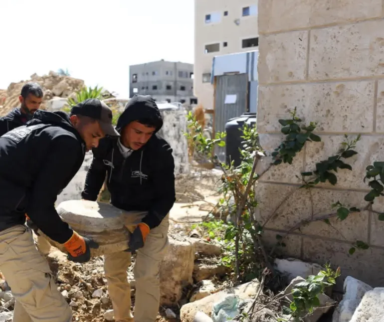 Members of the "Guardians of Heritage" team inspect and clean recovered archaeological pottery inside a temporary storage tent in Al-Mawasi, southern Gaza Strip. [Enas Naser/Al Jazeera]