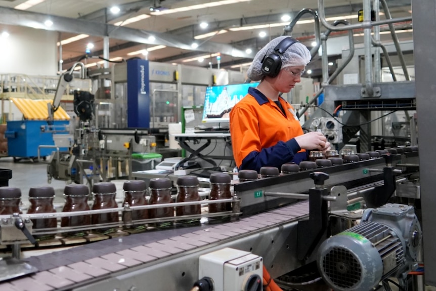 Woman in factory line with coffee jars on conveyor belt